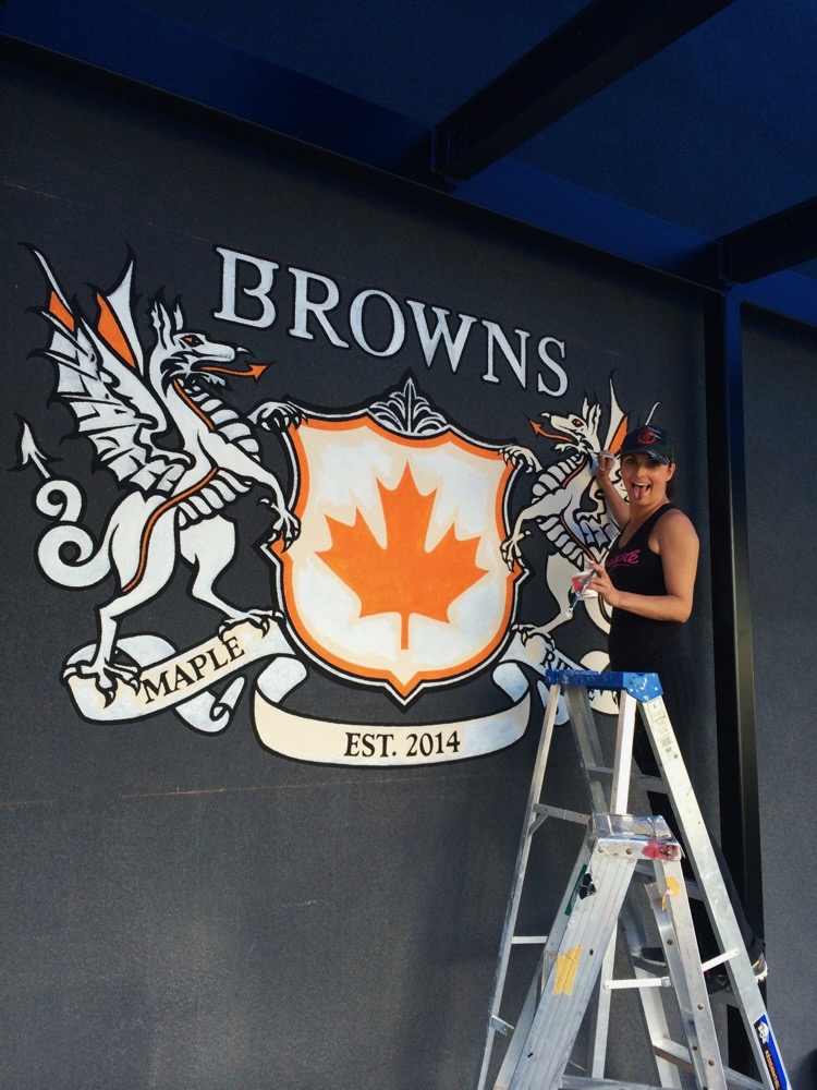Lina painting a Browns Social House mural from a ladder